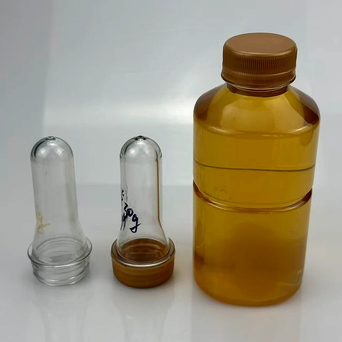 PET preform alongside a filled edible oil bottle and its cap